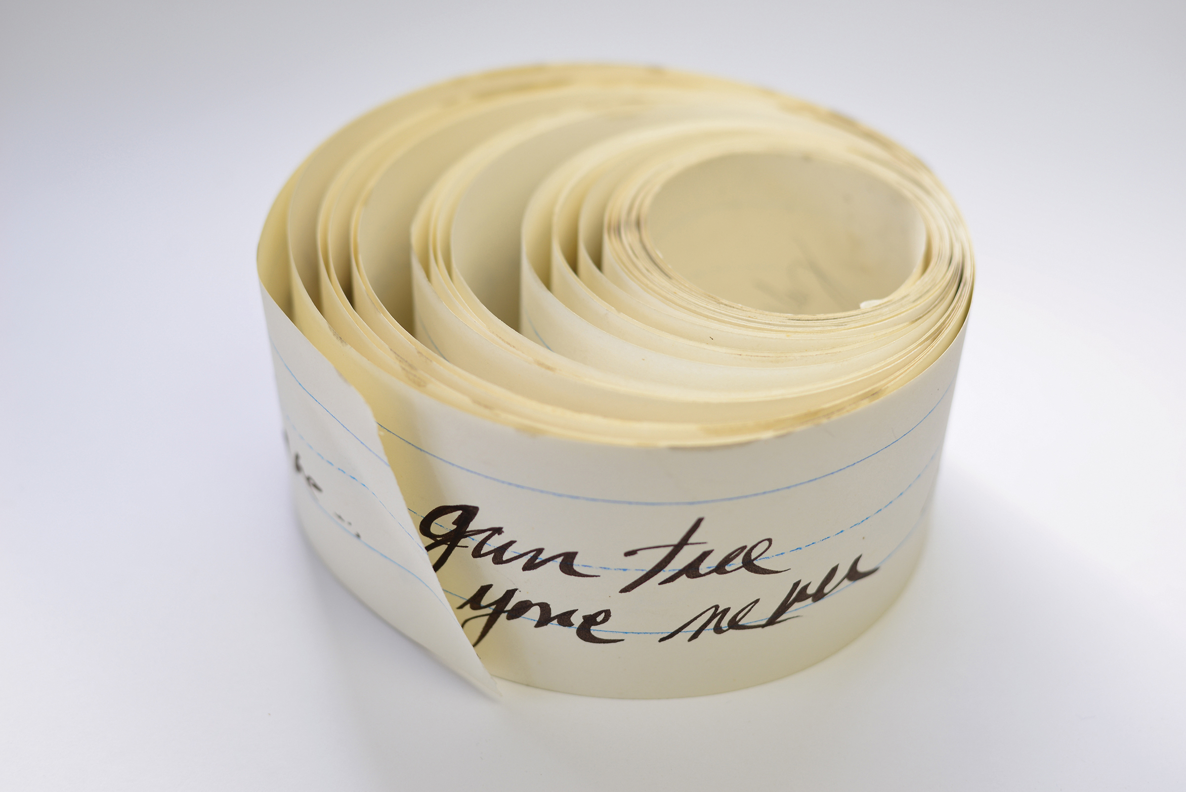 A narrow roll of white, lined paper with text handwritten on it in black ink.