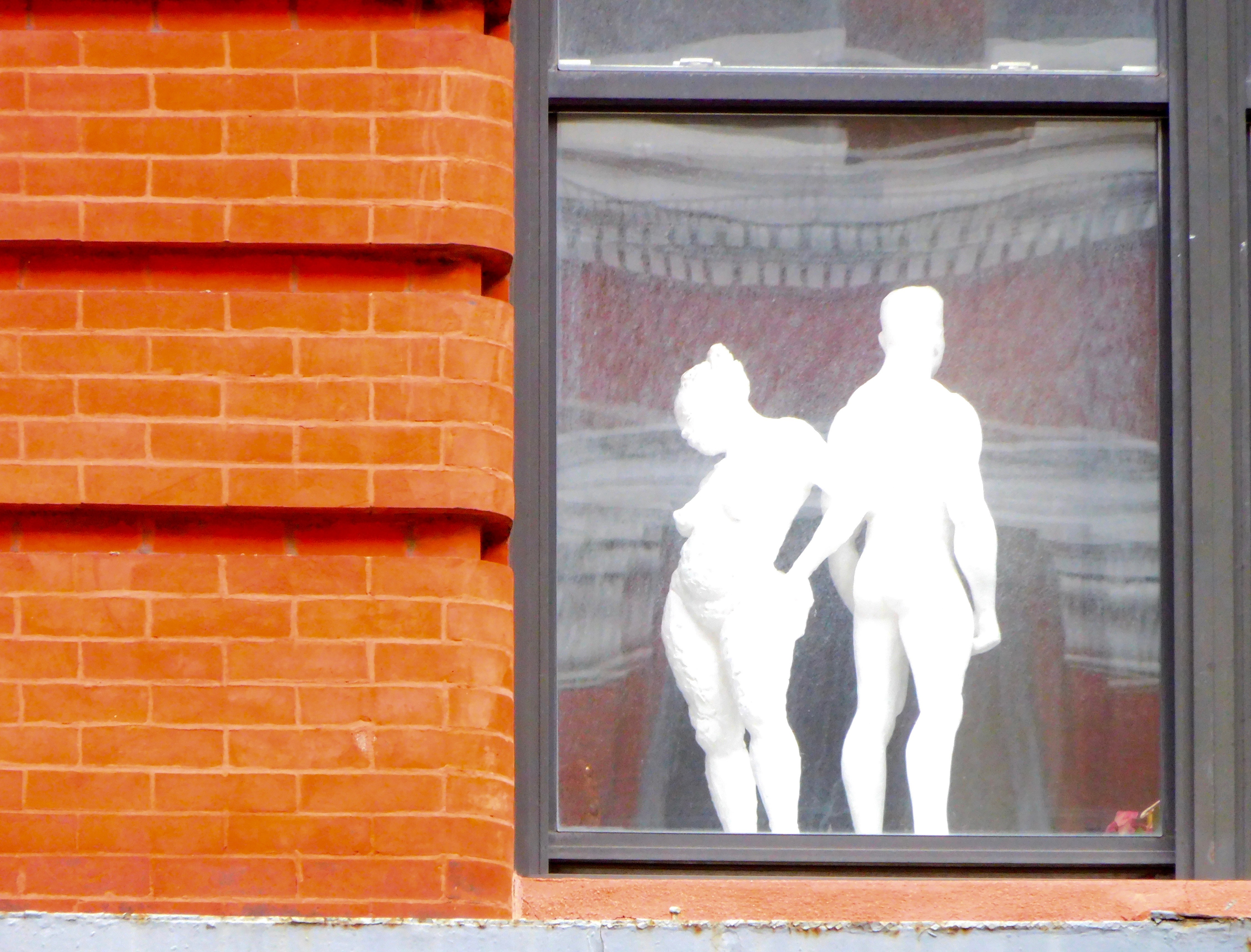 Two silhouettes stand in the window of a brick building.