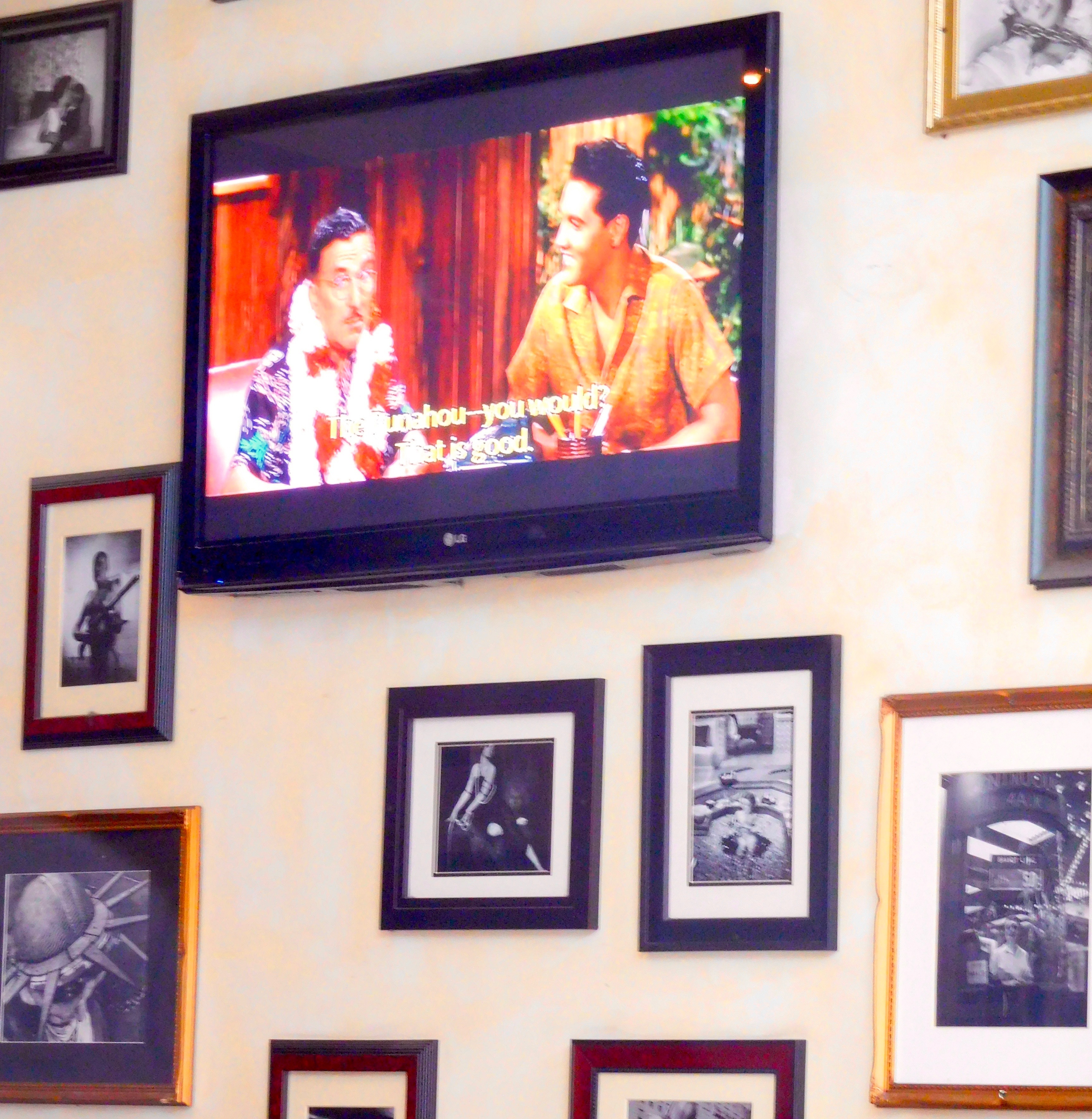 A TV is mounted on a wall amidst several framed photos