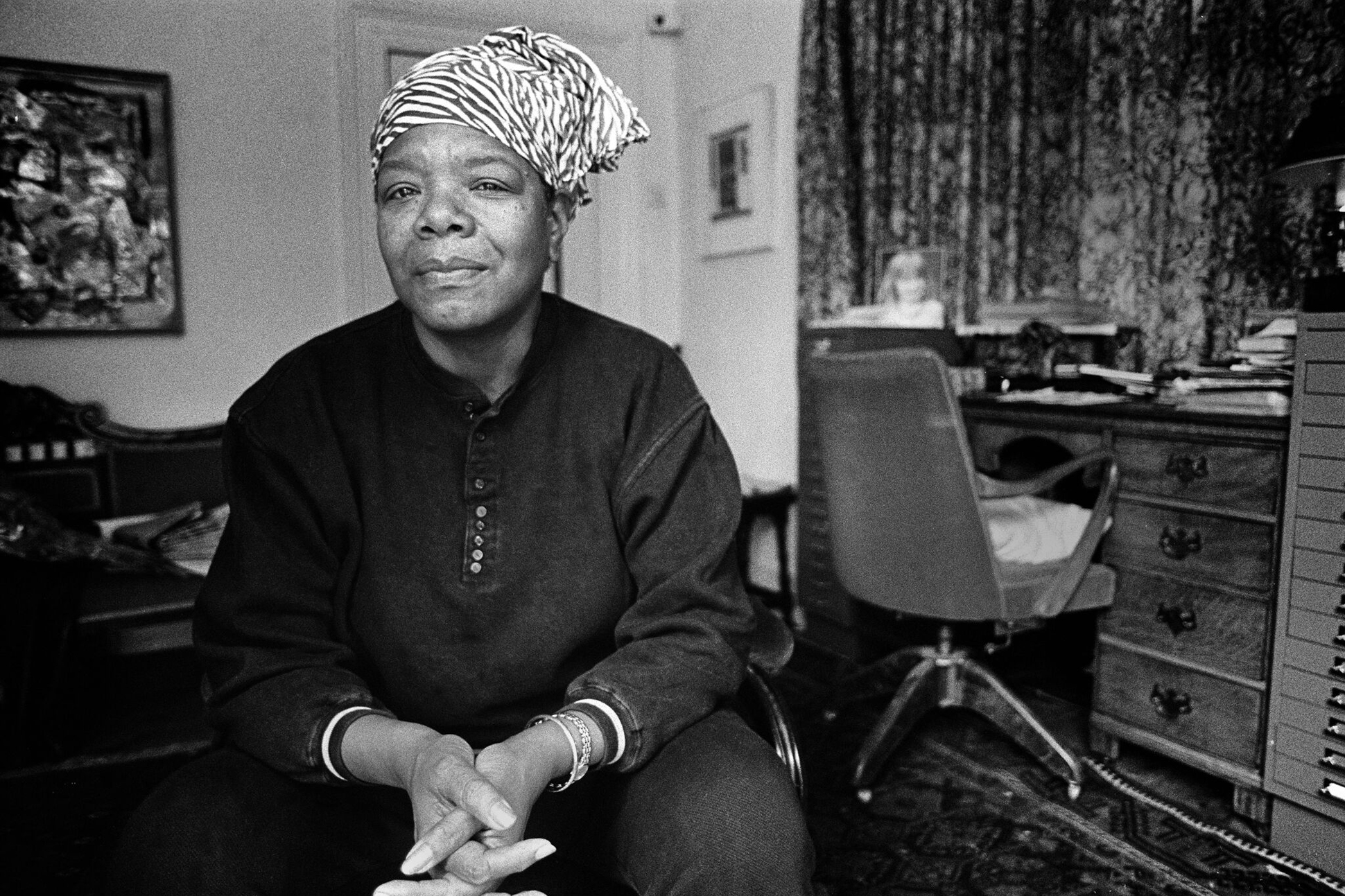 Black and white photograph of Maya Angelou, sitting with her hands clasped.