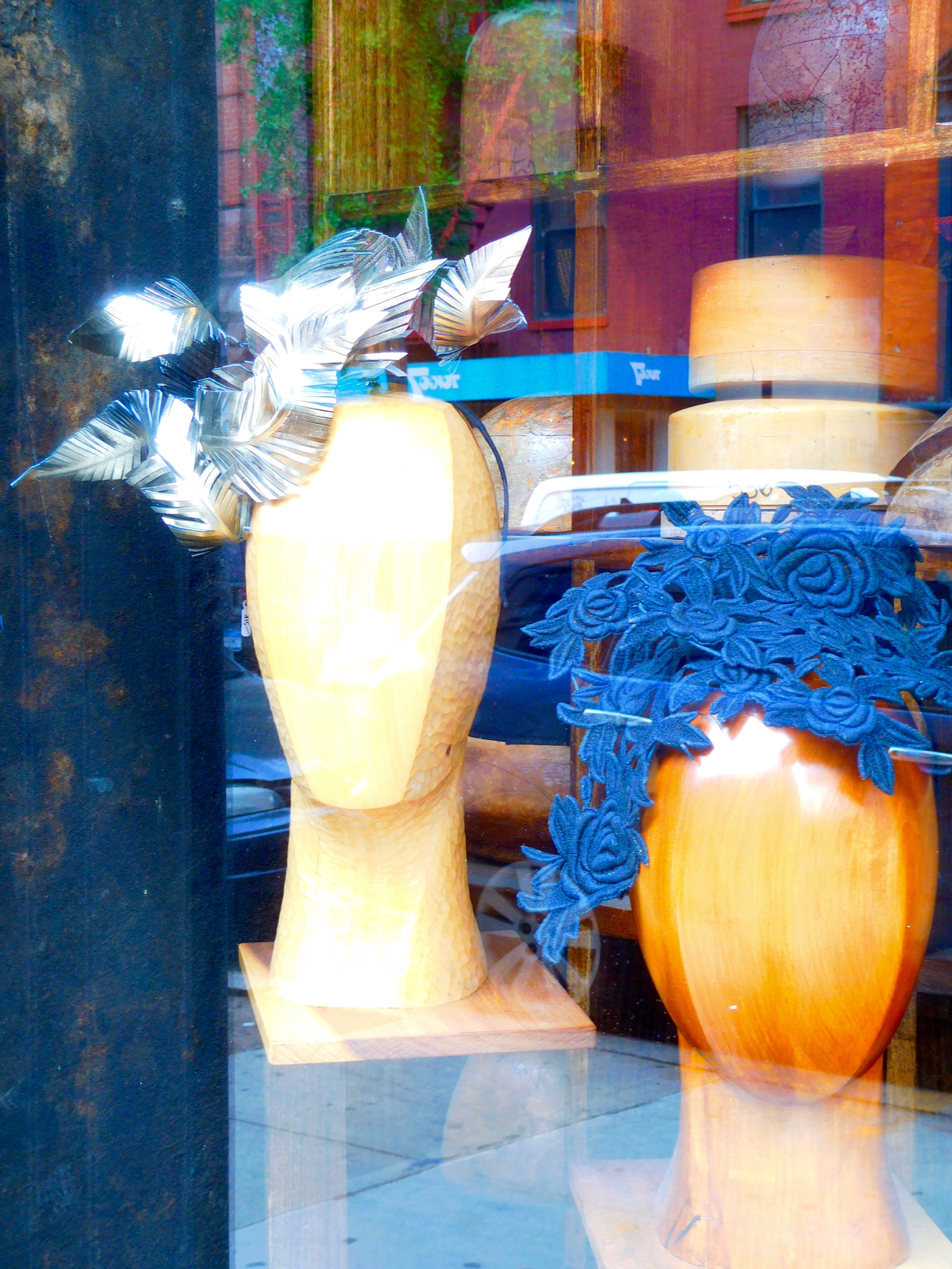 Two mannequin heads in a shop window wear artful headpieces.