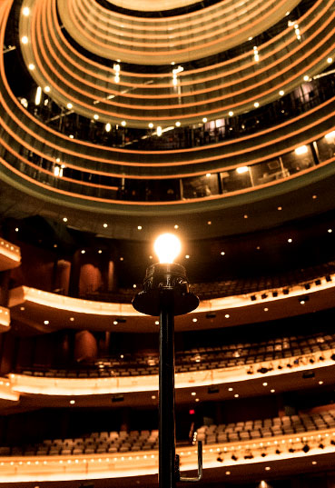 Looking out from behind a singular illuminated light bulb on the Schuster Center stage