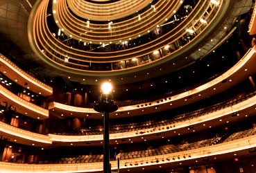 Looking out from behind a singular illuminated light bulb on the Schuster Center stage