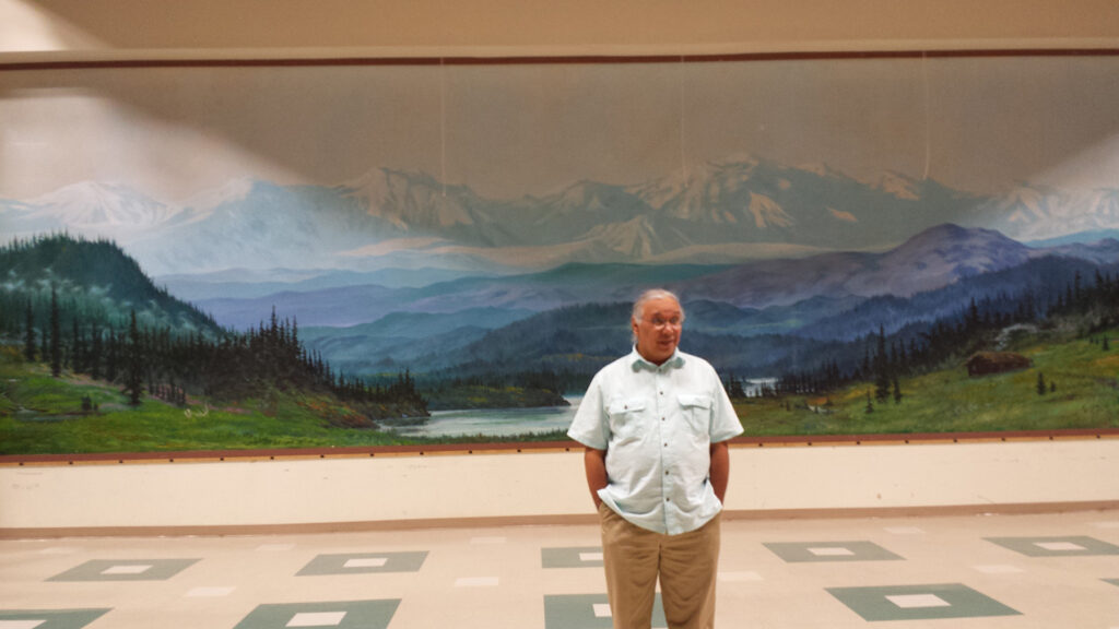 Photo of a man standing in front a mural of a mountain