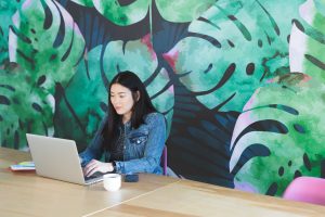 Woman working in an office on her laptop with a leaf mural on the wall behind her