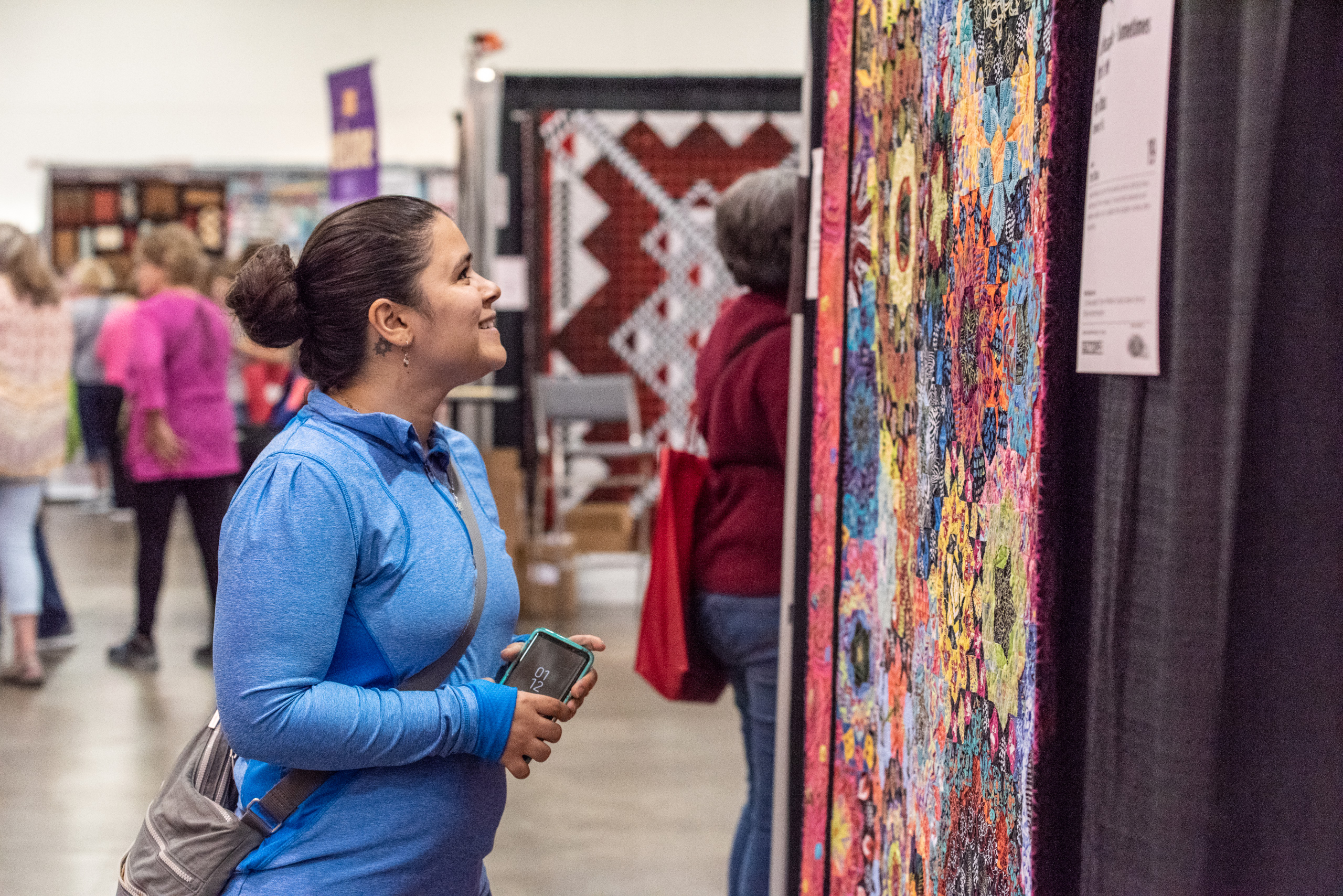 An attendee smiles while admiring a quilt in the Quilt Expo Quilt Exhibit.