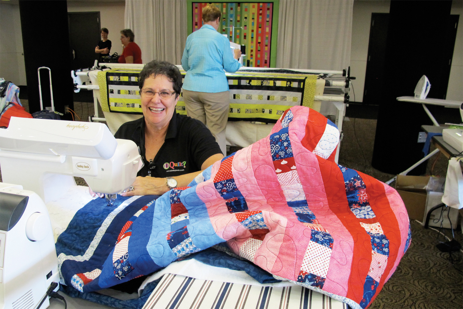 An attendee smiling at the camera while sewing at Quilt to Give at Quilt Expo.