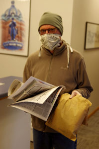 Man wearing face mask and hat and holding newspapers