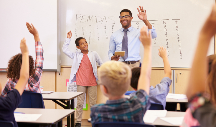 male teacher standing in front of an enthusiastic class of young students