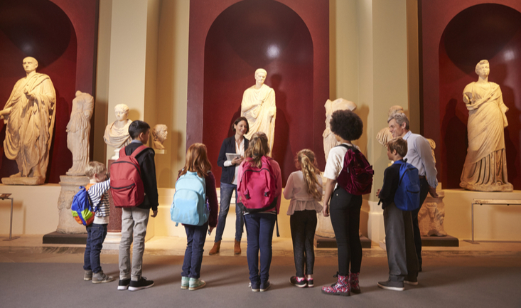 teacher in front of students at a museum standing in front of statues of ancient philosophers